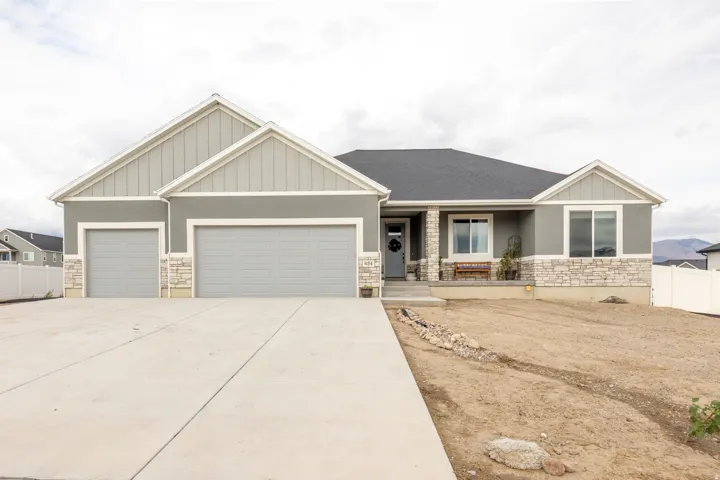 Single-story stucco exterior with stone accents, featuring a three-car garage, covered porch, and concrete driveway