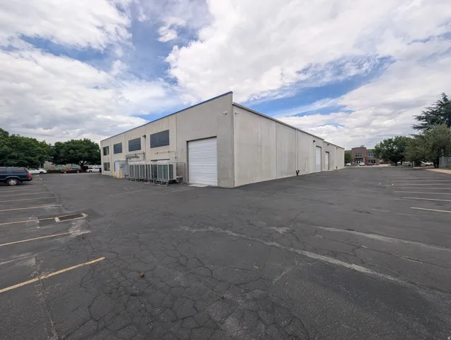 Commercial building featuring multiple roll-up doors, exterior HVAC units, and an expansive paved parking area