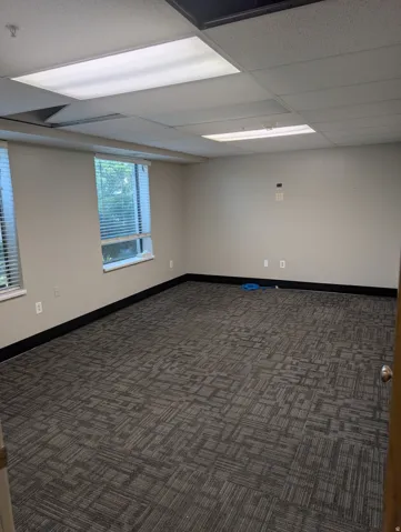 Textured carpet flooring, multiple windows with blinds, drop ceiling with recessed lighting, light-toned walls
