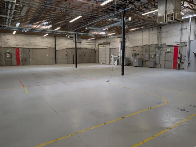 Spacious open-concept interior featuring concrete flooring, exposed ceiling beams, and overhead fluorescent lighting