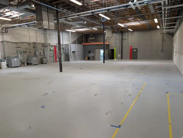 Expansive open floor plan with concrete flooring, exposed ceiling beams, ductwork, and fluorescent lighting