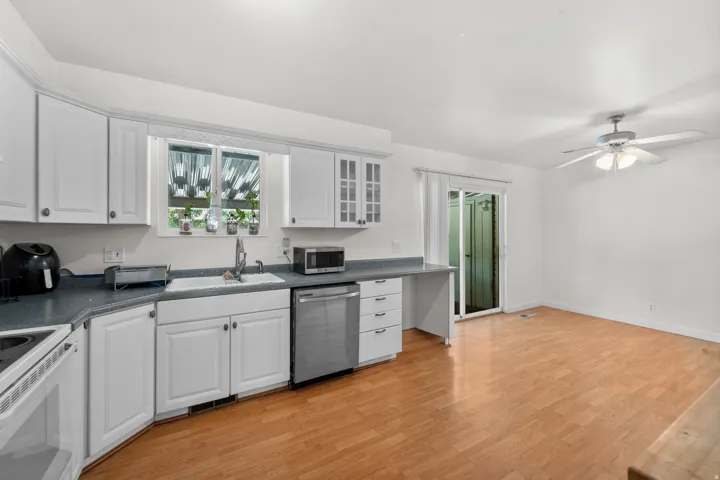 White cabinetry with glass-front accents, stainless steel dishwasher, wood-finish flooring, and a ceiling fan with integrated lighting