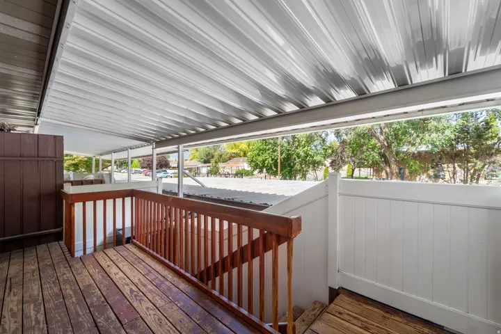 Covered outdoor deck with wood-finish flooring, wood railings, and a white privacy fence
