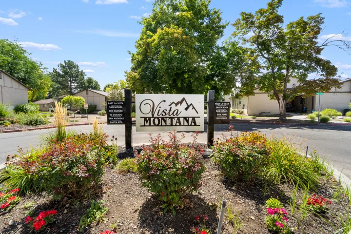 Landscaped entry featuring a welcome sign, mature trees, and shrubs