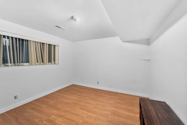 Wood-finish flooring with white baseboards, a window with vertical blinds, and a built-in corner shelf