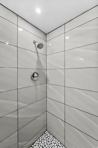 Recessed lighting, chrome shower fixture, large format wall tile, and a pebble tile shower floor
