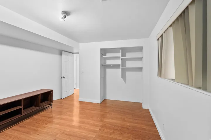 Recessed closet with integrated shelving, wood-finish flooring, white walls, and window with vertical blinds