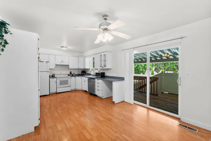Kitchen featuring white cabinetry, stainless steel appliances, wood-finish flooring, a ceiling fan, and sliding glass doors opening to an outdoor deck