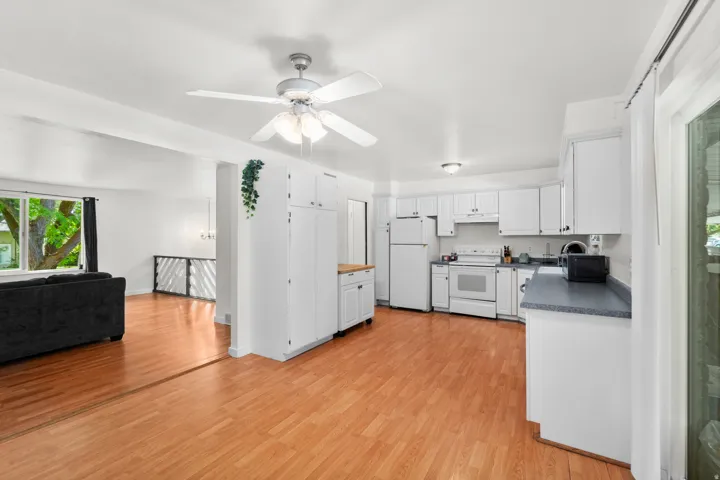 Open-concept living space featuring wood-finish flooring, white cabinetry, a ceiling fan, and white appliances