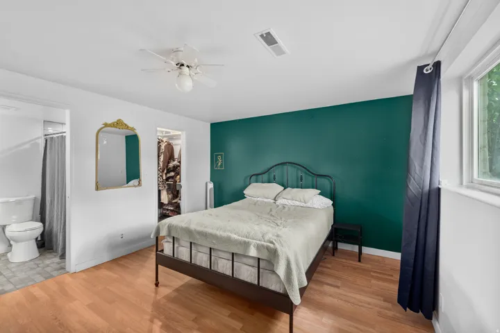 Wood-finish flooring, ceiling fan with light fixture, built-in closet, and an attached bathroom with toilet and shower
