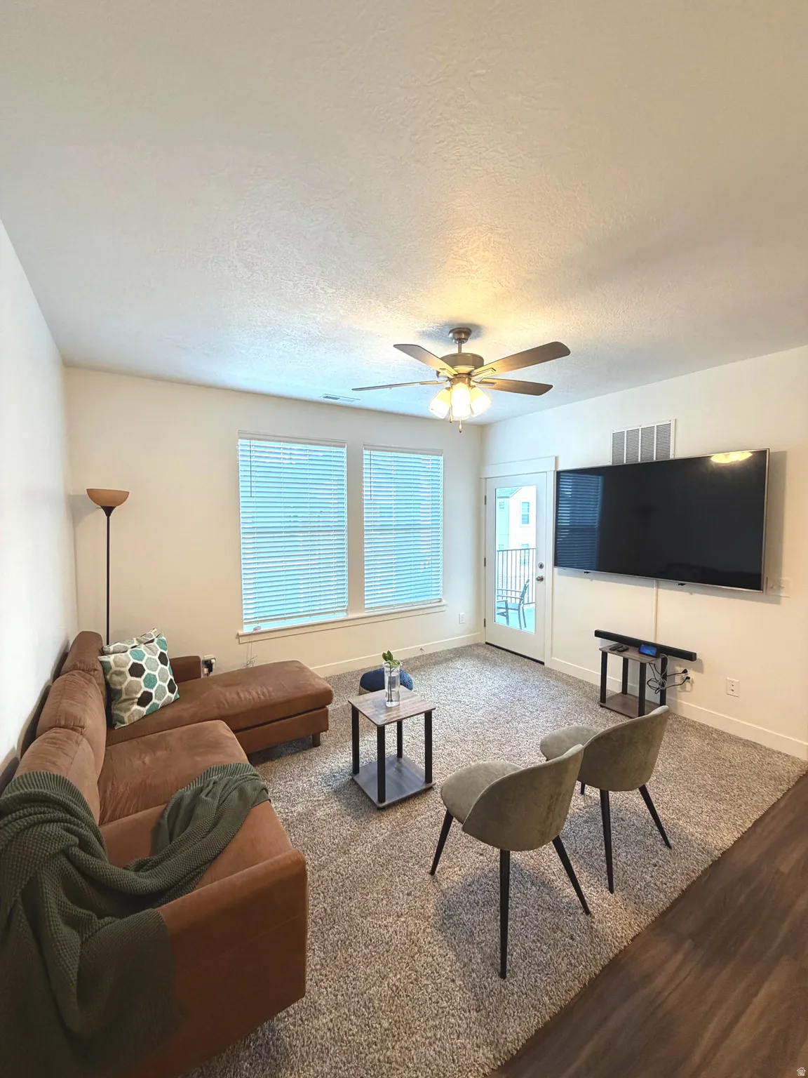 Carpeted living space with a ceiling fan, dual windows, and a glass-paneled door