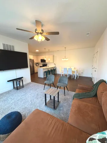 Open-concept living area featuring a ceiling fan with integrated lighting, wood-finish flooring, recessed lighting, and white cabinetry