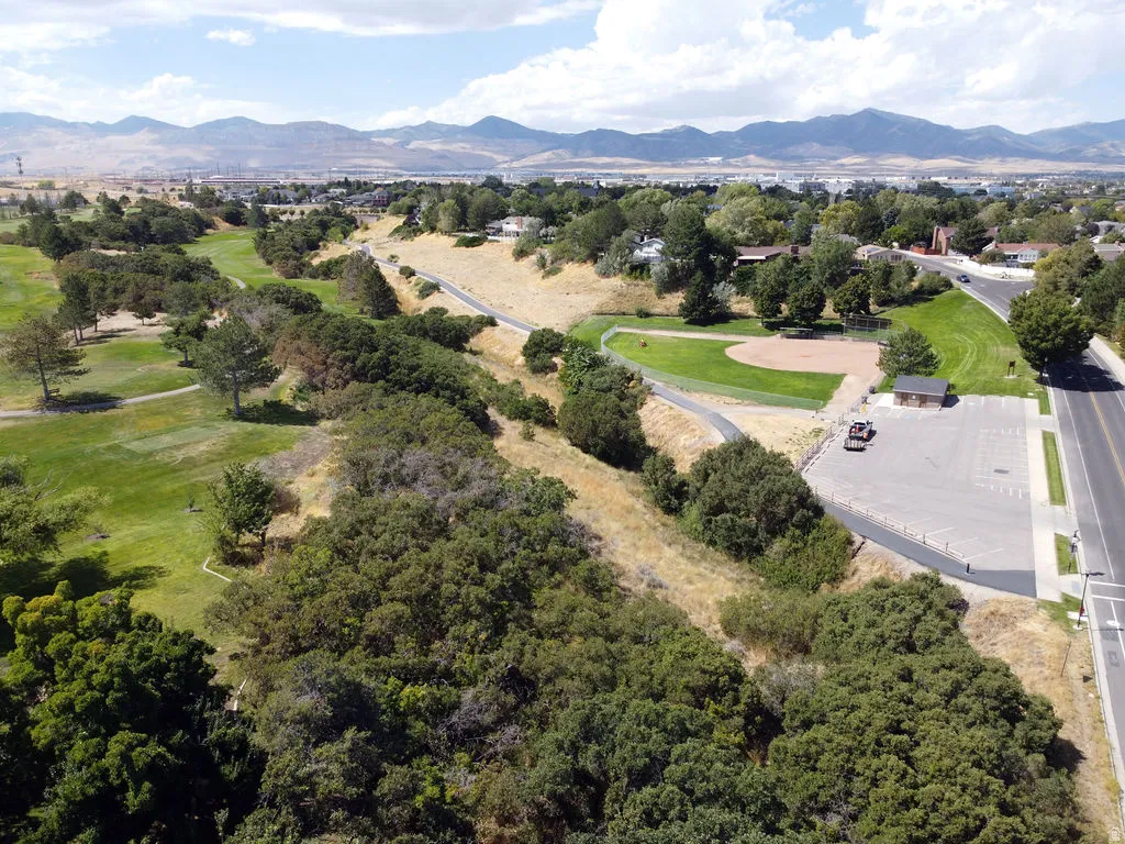 Expansive green space featuring a golf course, paved walking paths, a baseball field, and mountain scenery