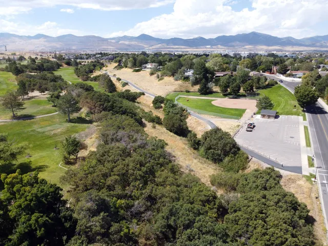 Expansive green space featuring a golf course, paved walking paths, a baseball field, and mountain scenery