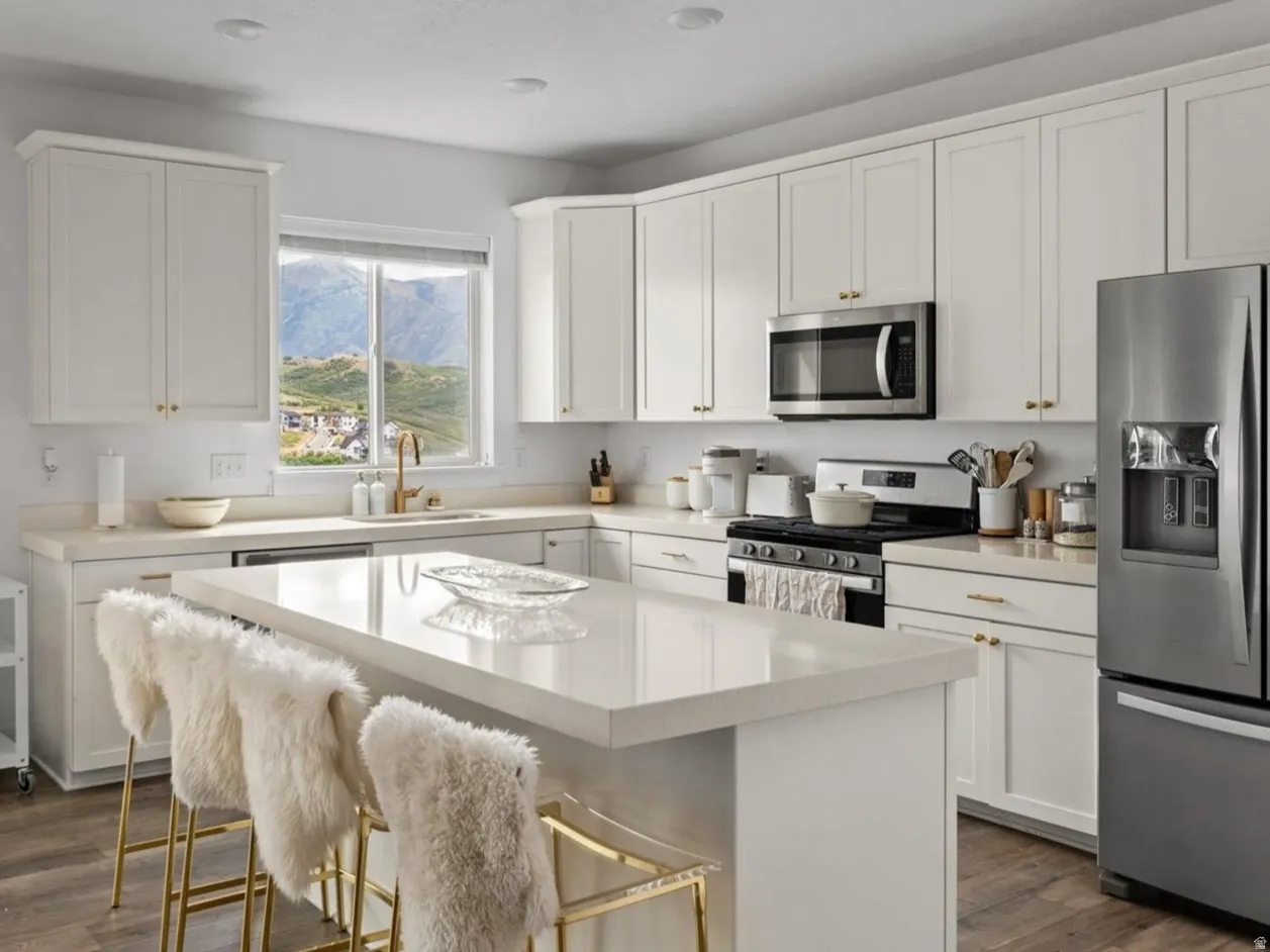 Contemporary kitchen featuring white cabinetry, stainless steel appliances, a center island with countertop seating, and wood-finish flooring