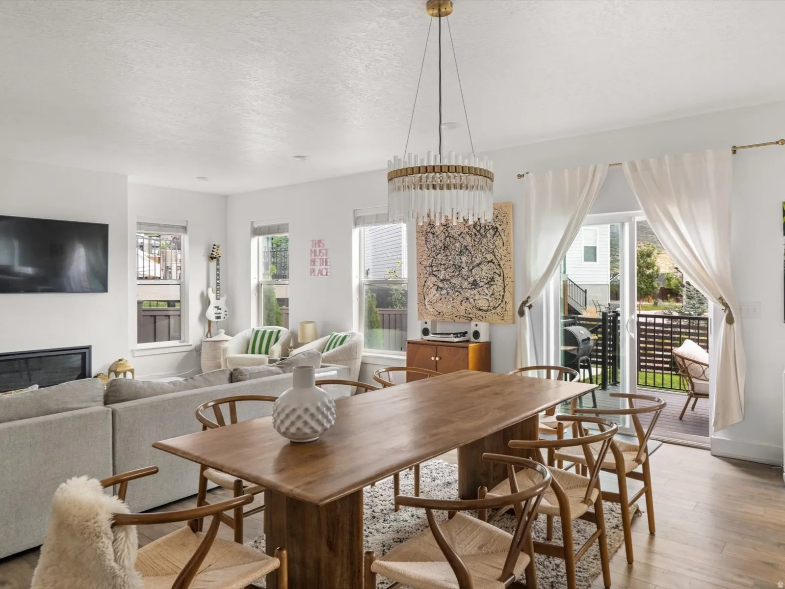 Open-concept living space featuring wood-finish flooring, a contemporary chandelier, a built-in fireplace, and sliding glass doors leading to an exterior balcony