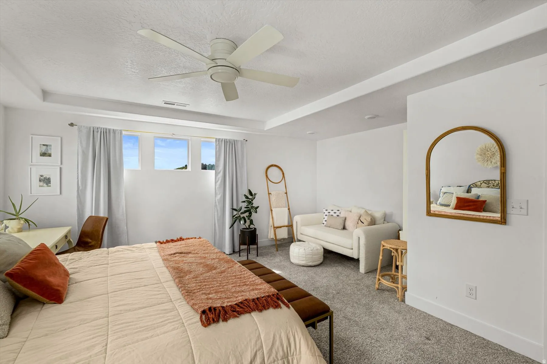 Recessed ceiling with integrated lighting, overhead ceiling fan, white walls, gray carpet flooring, and multiple high windows