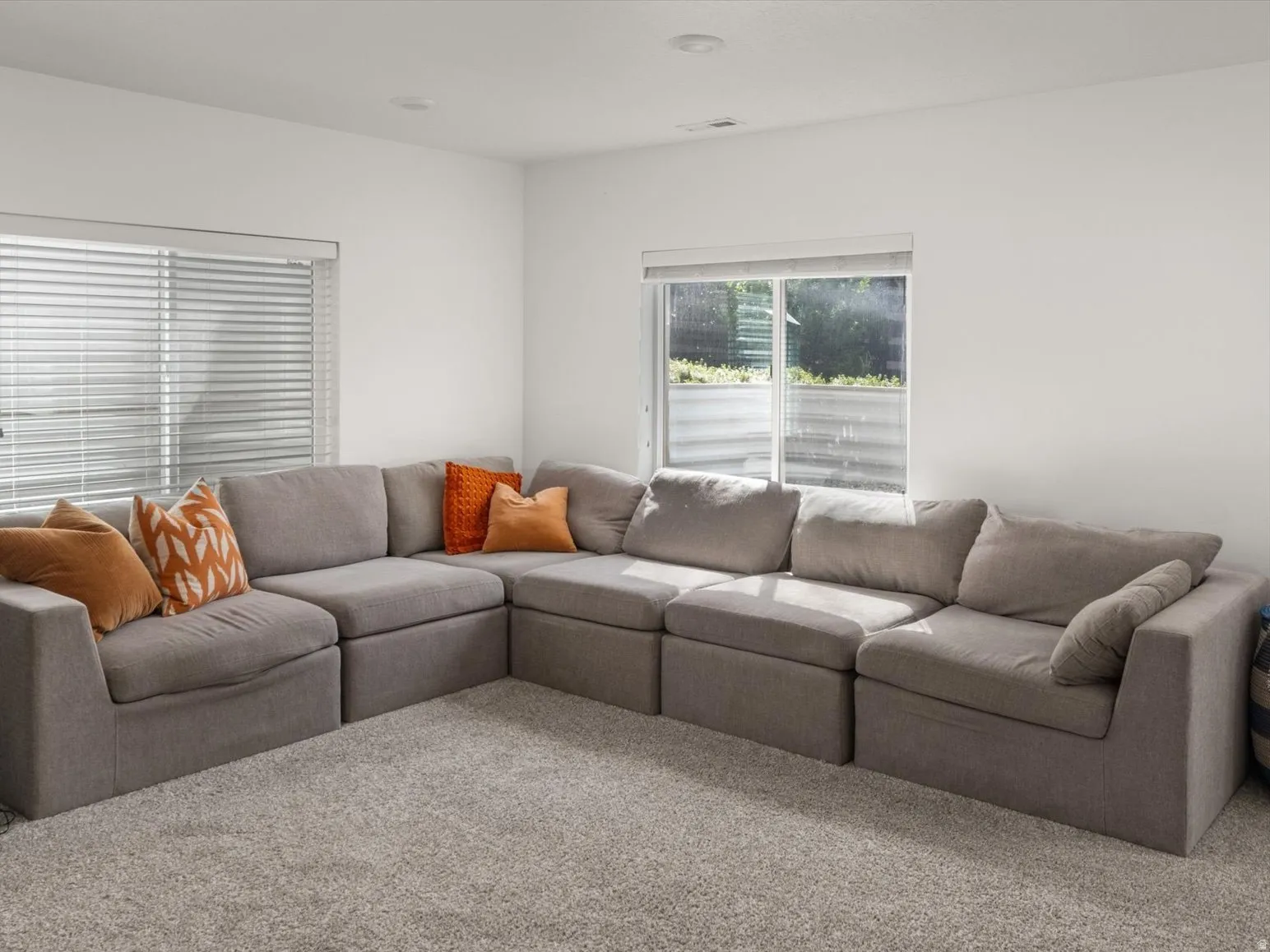 Recessed ceiling lighting, white walls, two windows with blinds, and light-colored carpet flooring