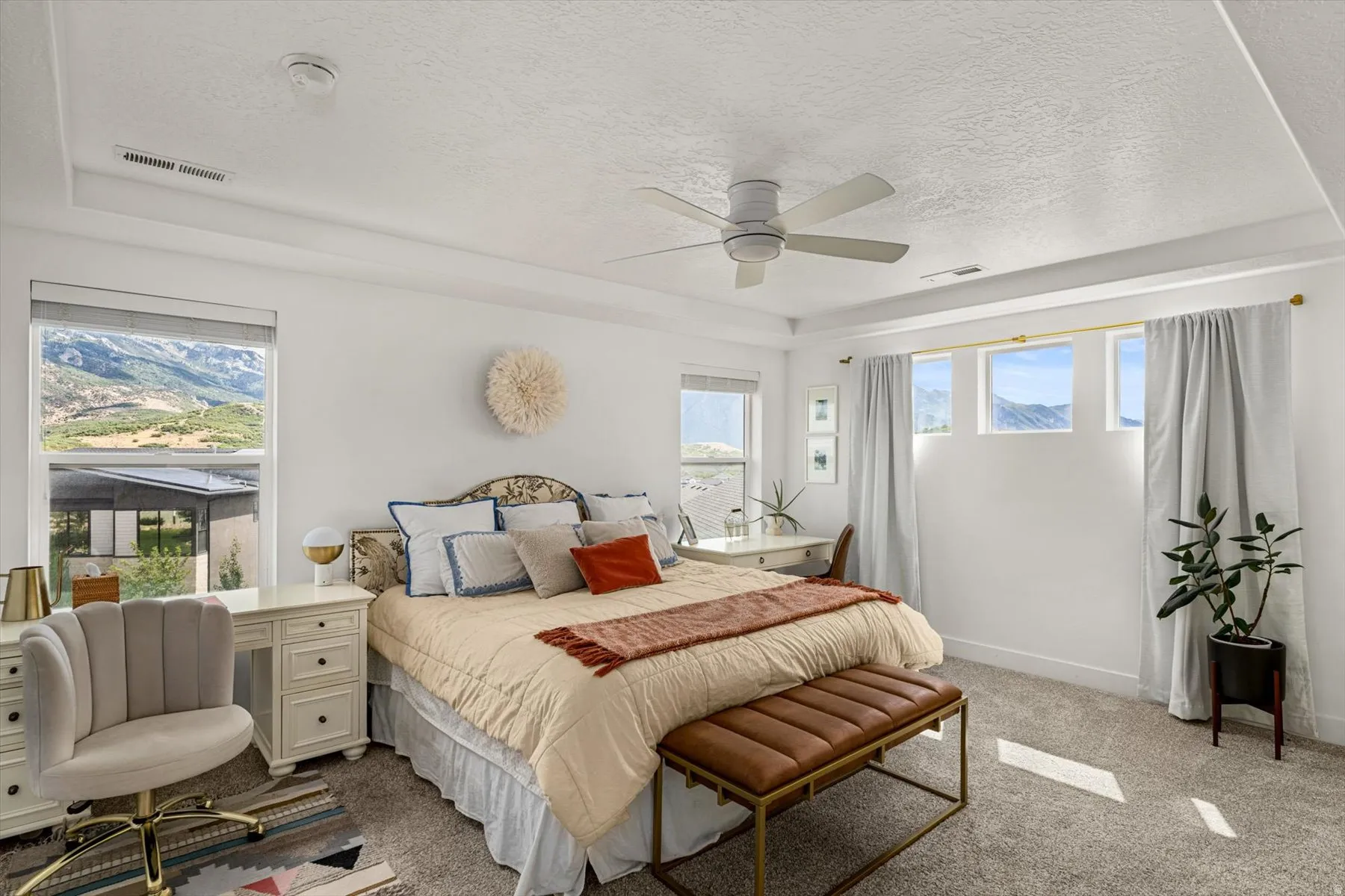 Recessed ceiling with a modern ceiling fan, large windows with scenic mountain backdrop, and light-colored carpeting