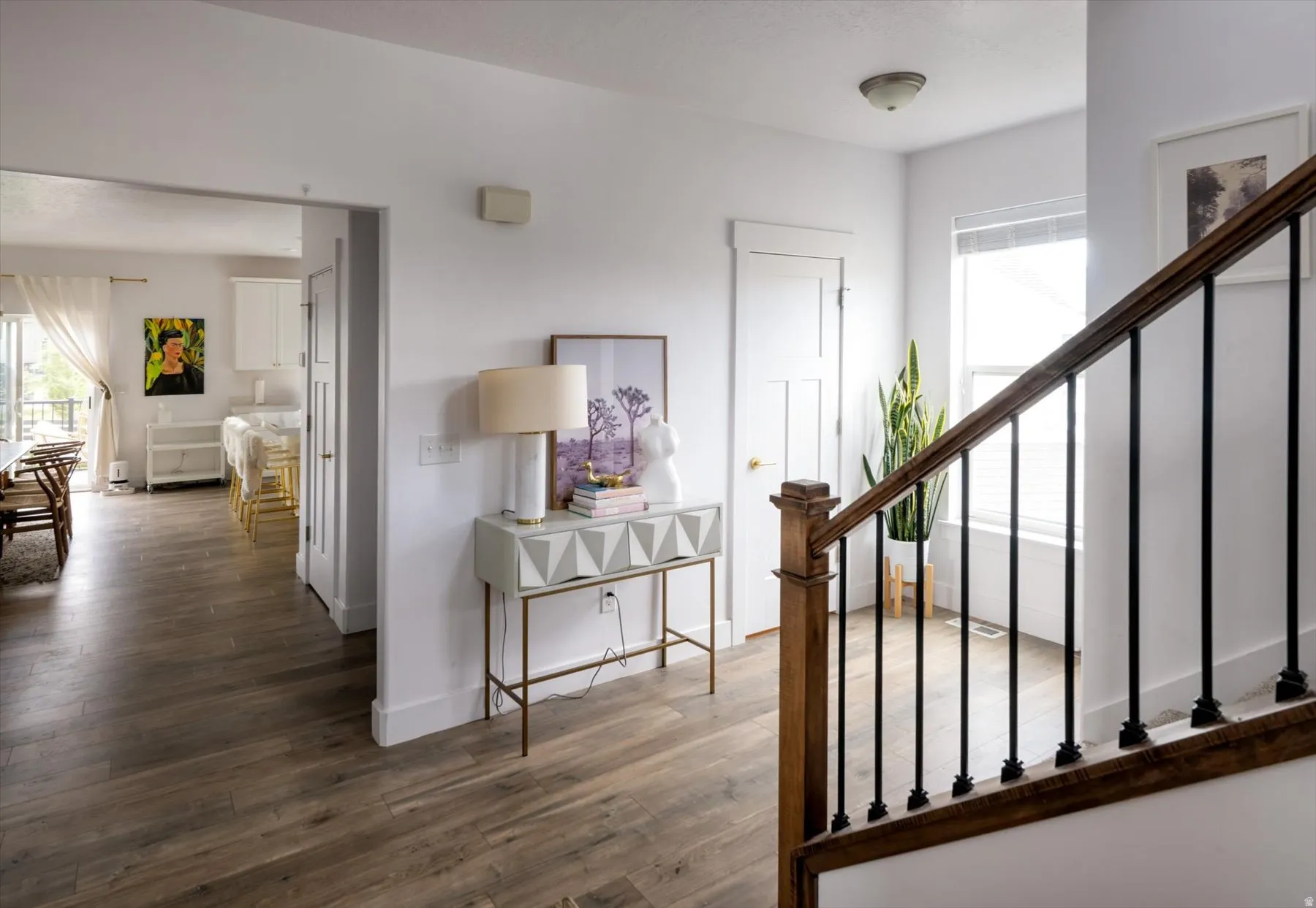Wood-finish flooring, white painted walls, wood staircase with black metal balusters, and a three-panel interior door
