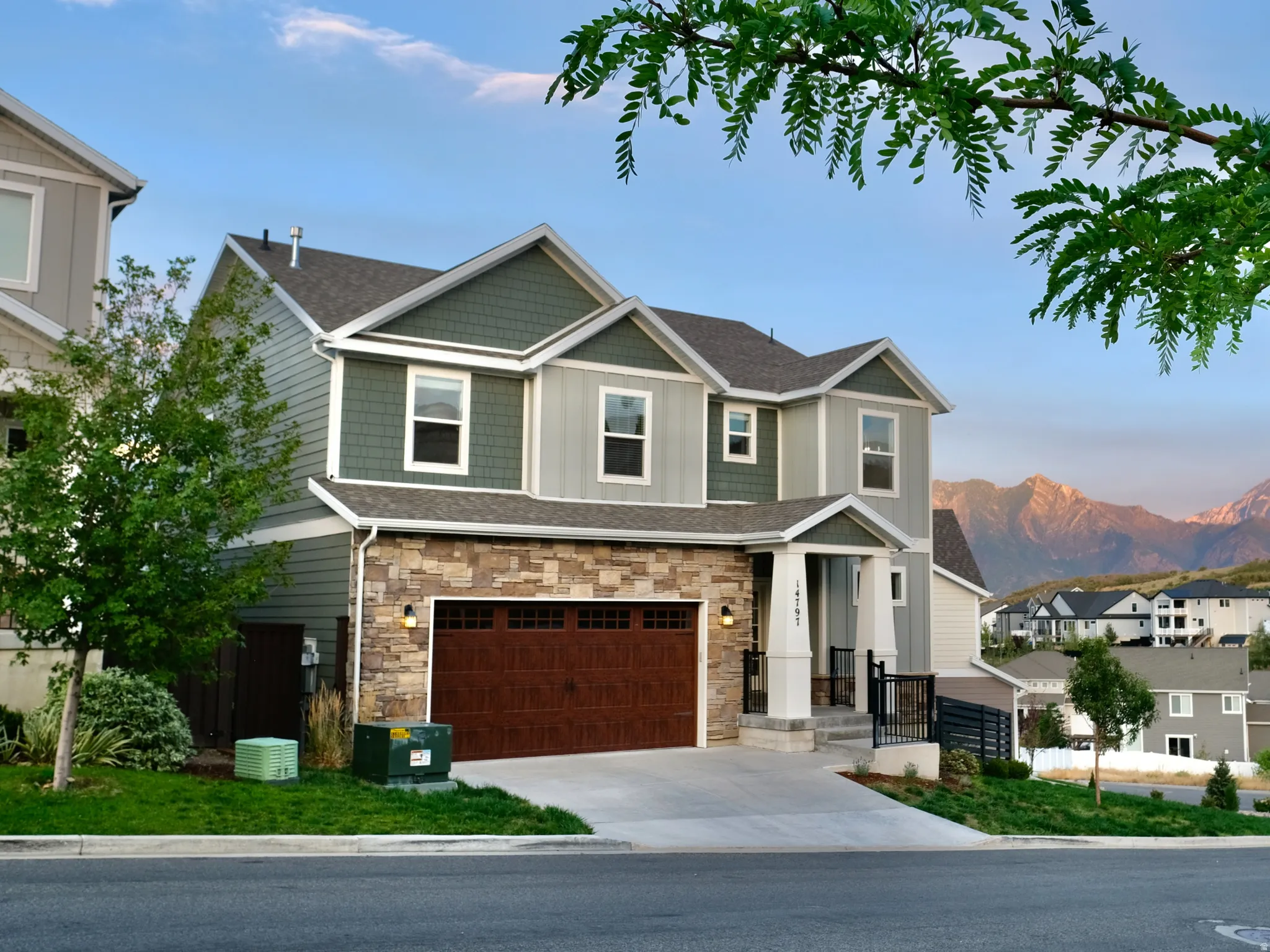 Two-story dwelling featuring a multi-toned exterior with stone and siding, an integrated garage with a wood-finish door, and a concrete driveway