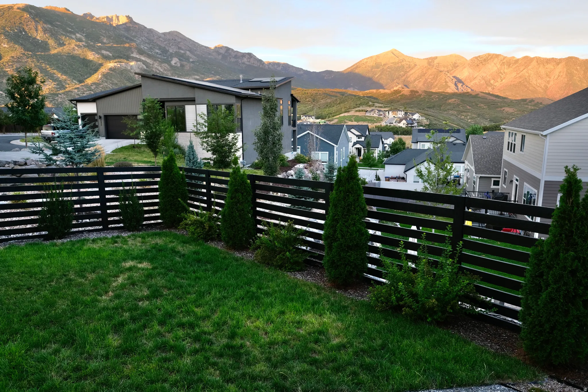 Manicured lawn with a modern horizontal slat fence, established evergreen landscaping, and expansive mountain scenery