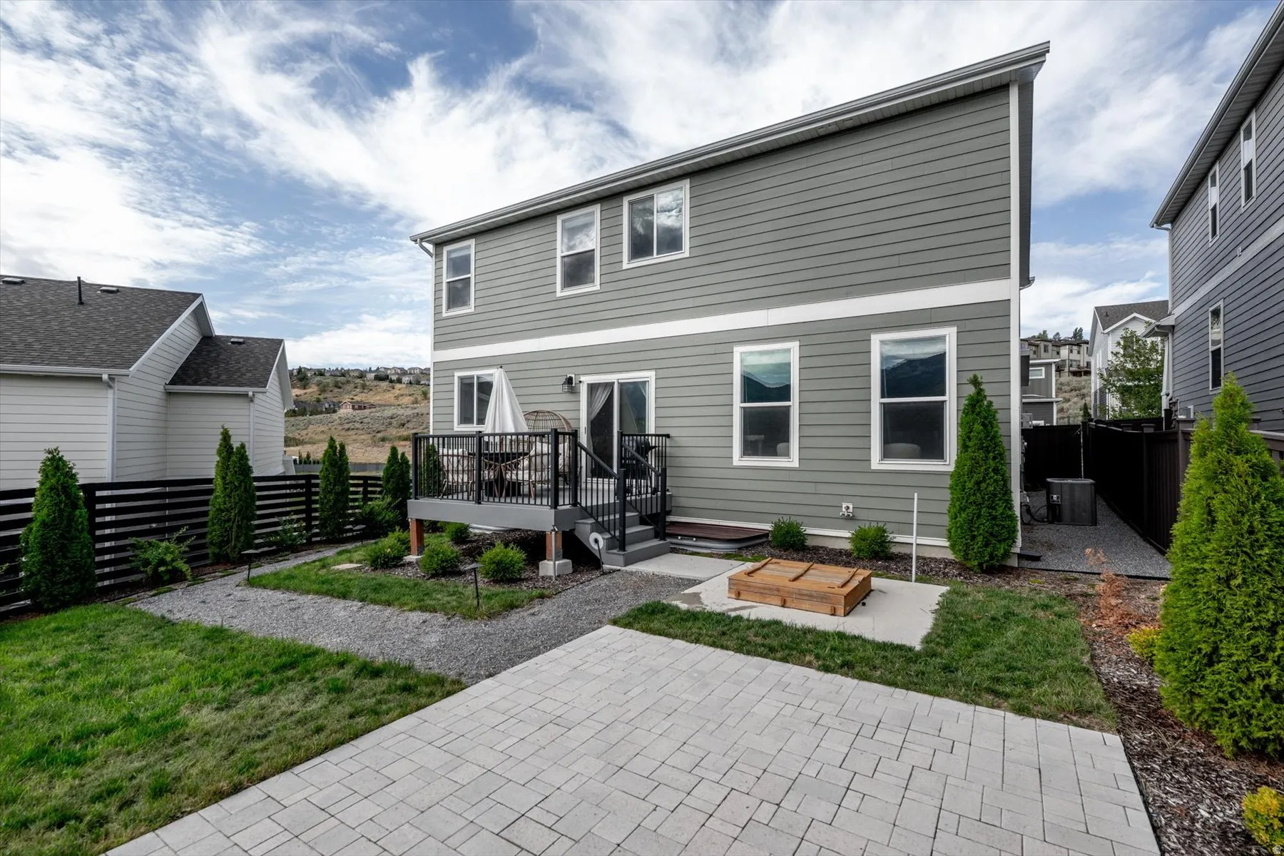 Rear exterior with two stories of siding, an elevated deck with black railings, a sliding glass door, a ground-level paver patio, and a privacy fence