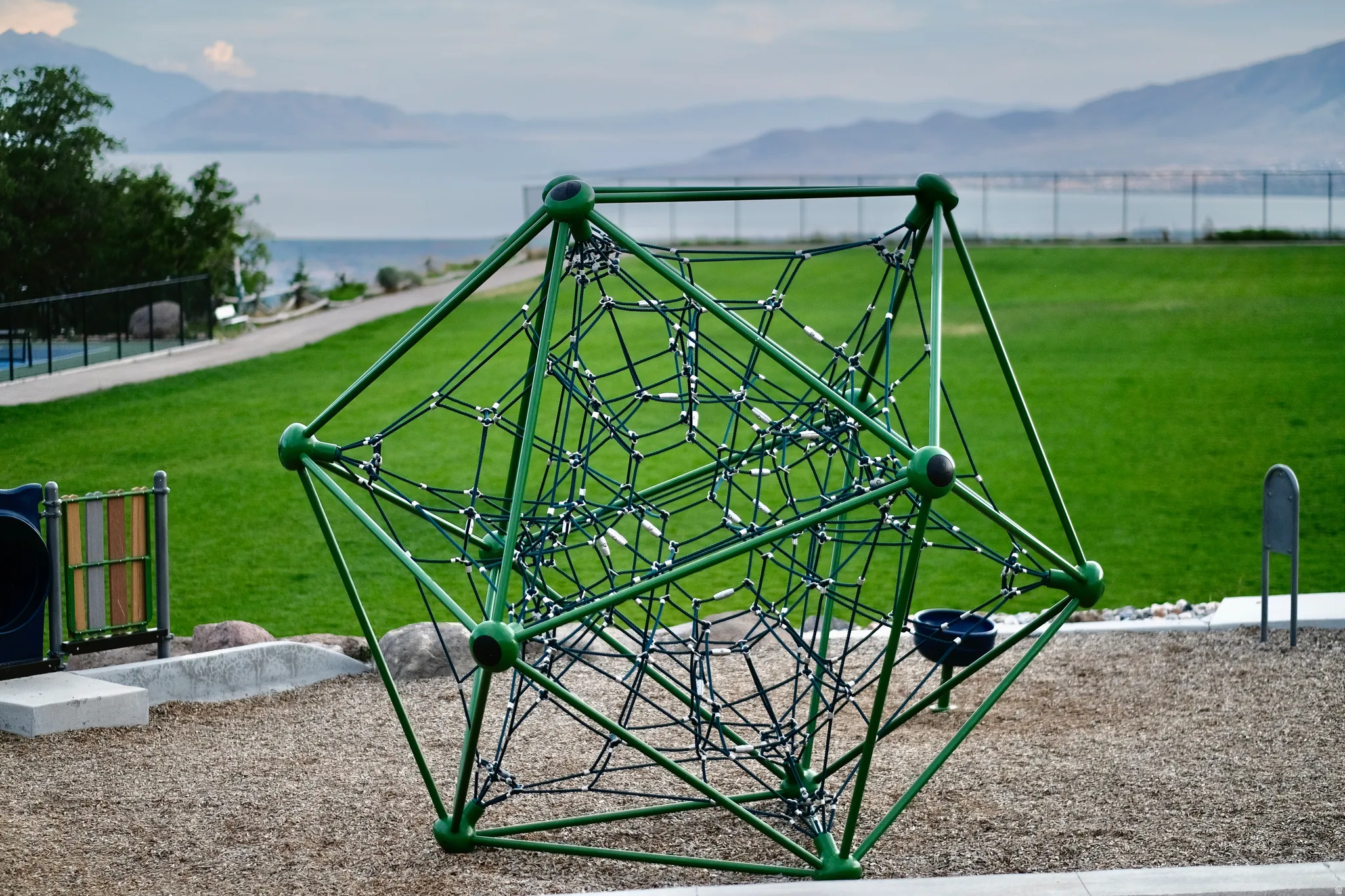 SunCrest Park climbing structure set on landscaped recreational grounds, with open lawn and scenic views toward Utah Lake.