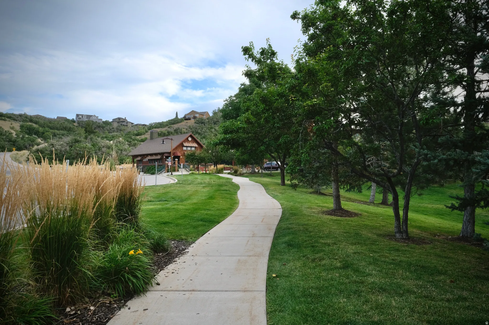 Curved concrete pathway leading to the SunCrest restaurant, surrounded by manicured lawns, mature trees, landscaped plantings, and hillside homes.