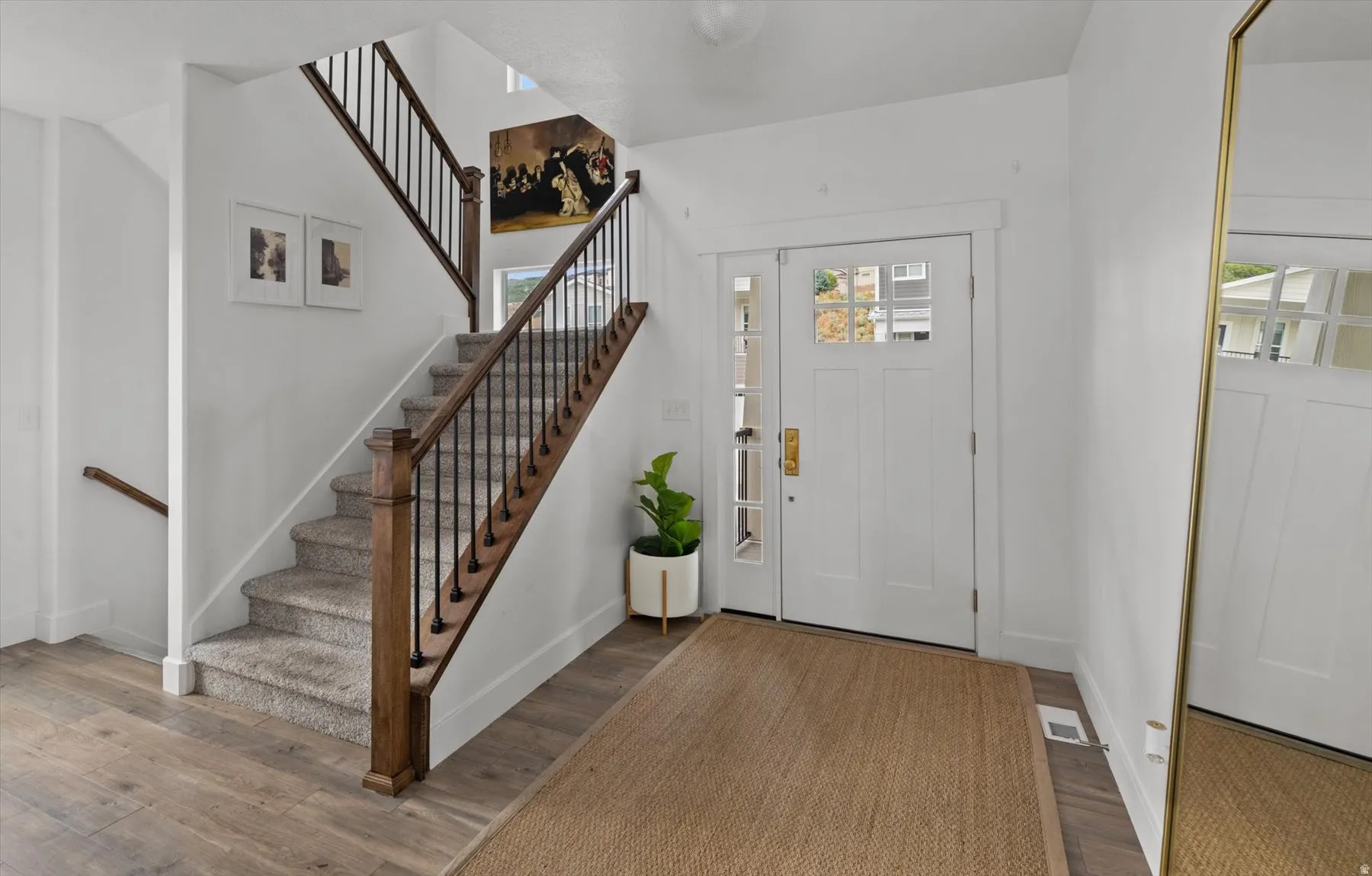 Craftsman-style entry door with glass panels, wood-finish flooring, and a staircase featuring wood newel posts, handrails, and black metal balusters