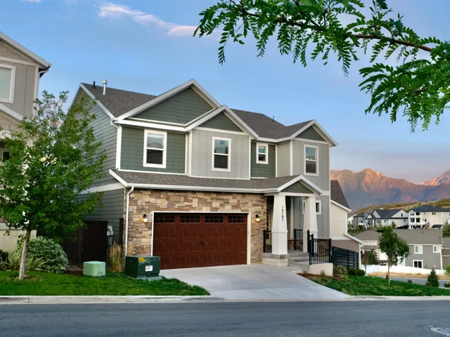 Two-story dwelling featuring a multi-toned exterior with stone and siding, an integrated garage with a wood-finish door, and a concrete driveway