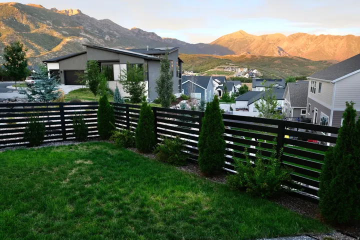 Manicured lawn with a modern horizontal slat fence, established evergreen landscaping, and expansive mountain scenery