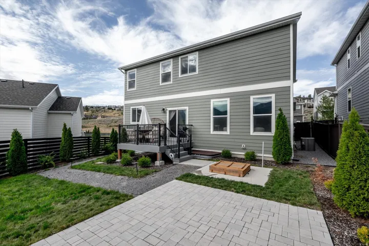 Rear exterior with two stories of siding, an elevated deck with black railings, a sliding glass door, a ground-level paver patio, and a privacy fence