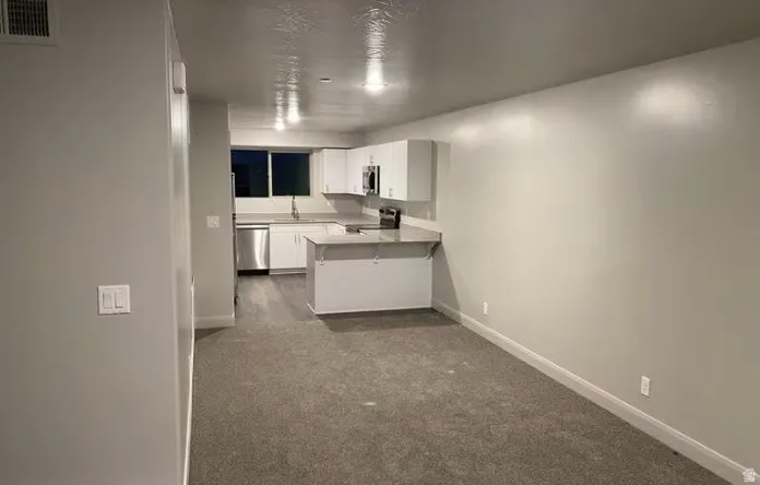 Kitchen area with white cabinetry, stainless steel appliances, and a breakfast bar