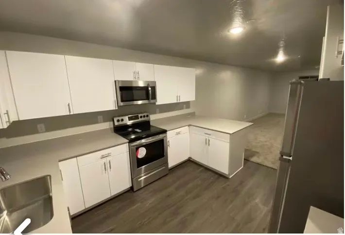 Kitchen featuring white cabinetry, light-toned countertops, stainless steel appliances, and wood-finish flooring