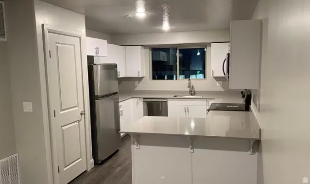 Kitchen featuring white cabinetry, stainless steel appliances, a window above the sink, light-toned countertops, and wood-finish flooring