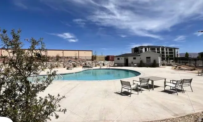 Curved swimming pool with a concrete surround, surrounded by a building with light-colored siding and a dark roof