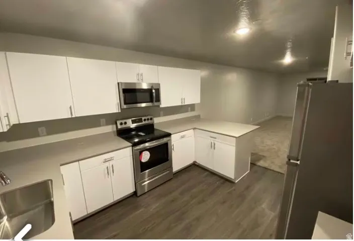 Kitchen featuring white cabinetry, light-toned countertops, stainless steel appliances, and wood-finish flooring