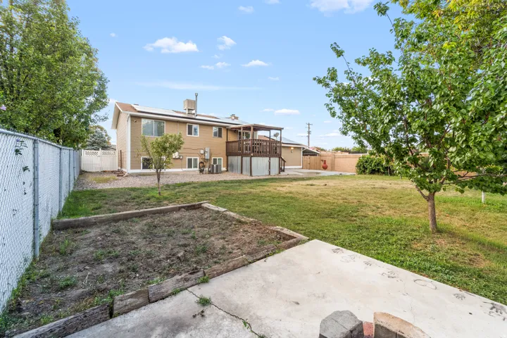 Expansive backyard with a covered deck, chain-link fencing, and mature trees
