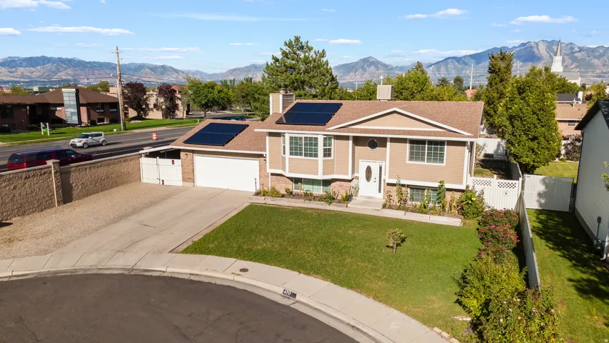 Split-level residence featuring a two-car garage, solar panels, and a front lawn