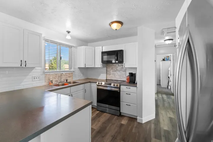 Kitchen featuring white shaker-style cabinetry, dark countertops, subway tile backsplash, and wood-finish flooring