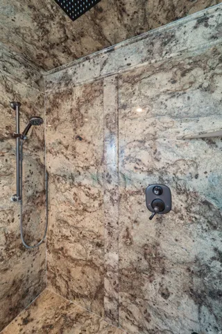 Walk-in shower with full-height stone-look tile, rain shower head, handheld shower fixture, and recessed shower niche
