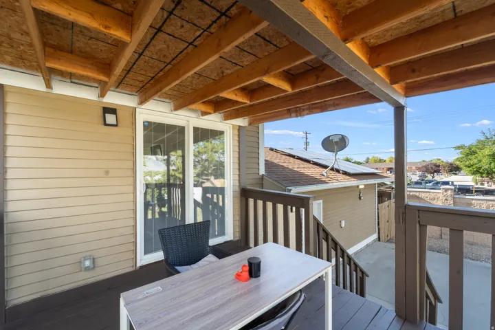Covered outdoor deck with exposed wood beam ceiling, wood-finish railing, and light tan siding