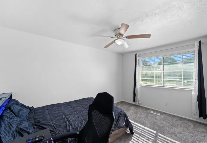 Window with horizontal blinds, ceiling fan with light fixture, and textured carpeting