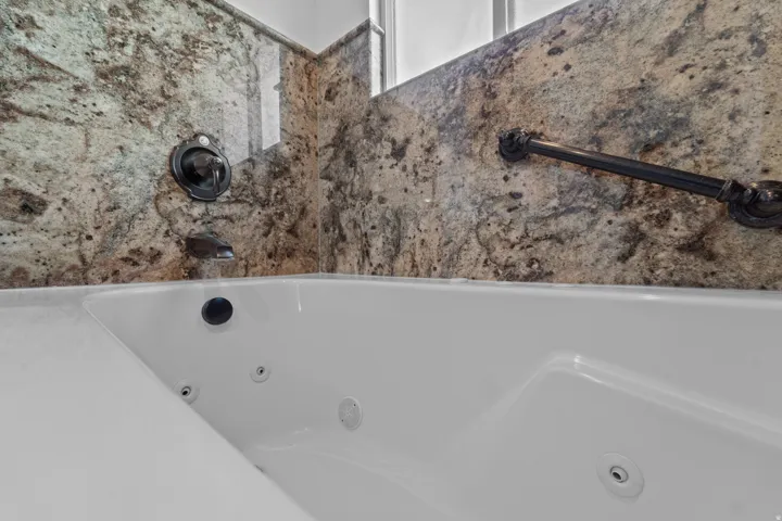 Jetted tub with a tiled surround, integrated fixtures, and a wall-mounted grab bar