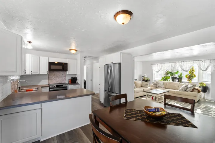 Kitchen featuring white cabinetry, a tile backsplash, stainless steel appliances, and a peninsula with dark countertops