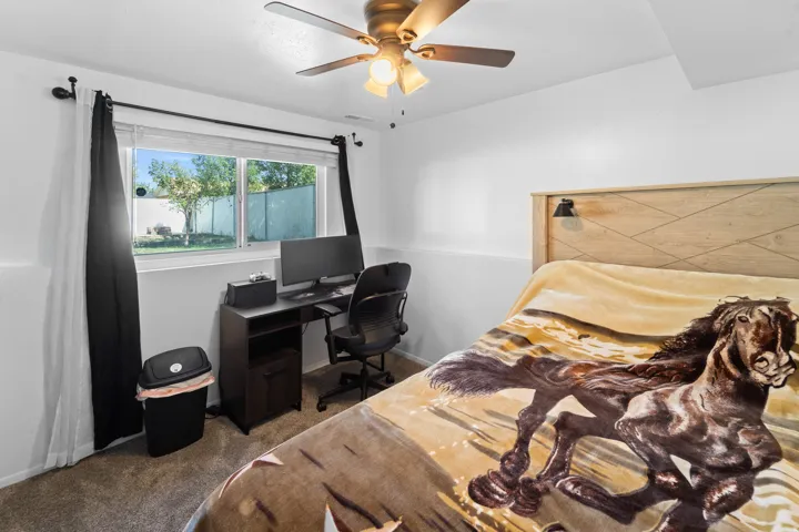 Bedroom featuring a ceiling fan with integrated lighting, wood-finish headboard, and a window providing natural light and exterior views