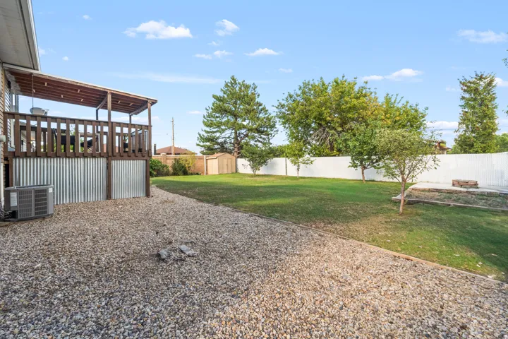Expansive backyard featuring a covered deck, gravel patio, manicured lawn, and perimeter fencing
