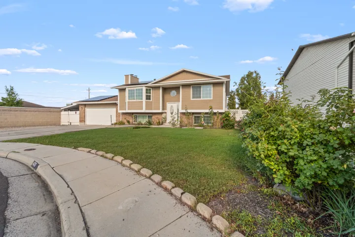 Split-level residence featuring a two-car garage, solar panels, and a stone-trimmed sidewalk