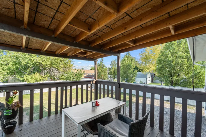 Covered outdoor deck with wood flooring and railing, featuring an exposed beam ceiling